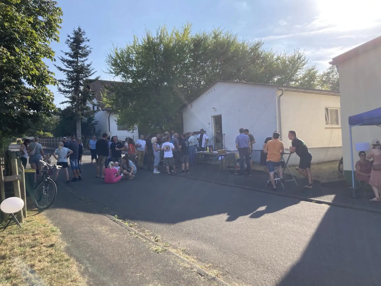 Viele Gäste stehen auf der Straße vor dem weiß verputzten Gefrierhaus in der Abendsonne