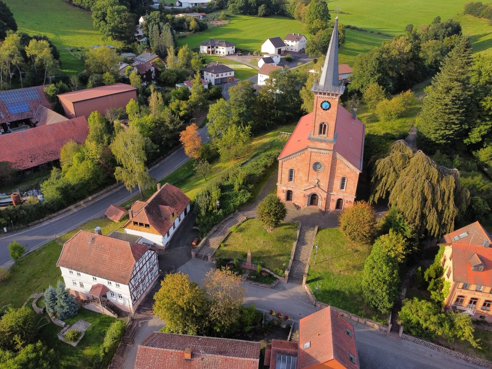 Die evangelische Kirche aus der Luft: roter Sandsteinbau mit Turm und Uhr, davor die Freitreppe