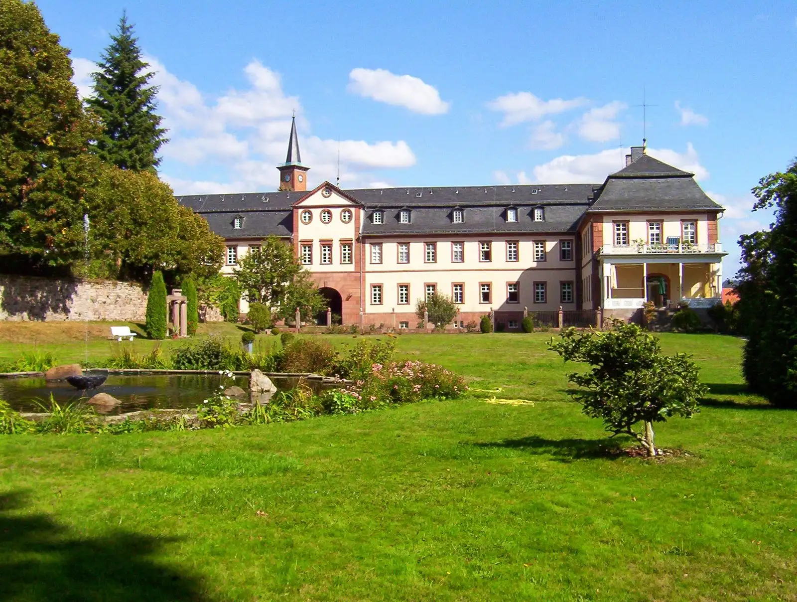 Schloss Stockhausen: langgestreckter Barockbau mit Uhrturm hinter einer Rasenfläche mit Teich