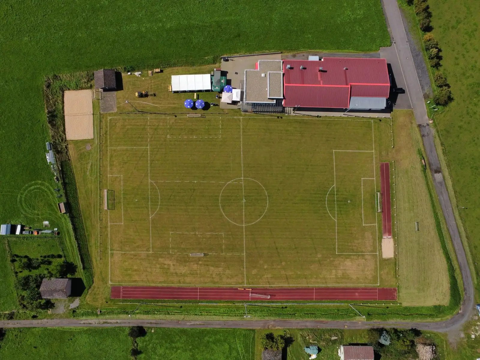 Der Sportplatz aus der Luft: Rasenplatz mit roter Laufbahn, daneben die Altfellhalle mit rotem Dach